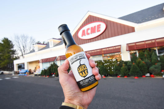 Picture of a hand holding a bottle of Sauce Bae skinny Habanero infant of an ACME grocery Store