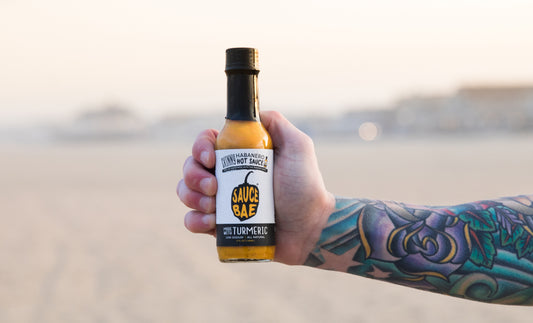 Picture of a tattooed arm holding a bottle of Sauce Bae Skinny Habanero Hot Sauce