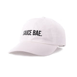 Angled view of white dad hat with white embroidered 'Sauce Bae' logo on the front. Perfect for fans of Sauce Bae, a health-focused hot sauce and raw honey brand