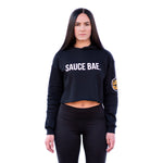 Brunette model wearing a black Sauce Bae Crop Hoodie